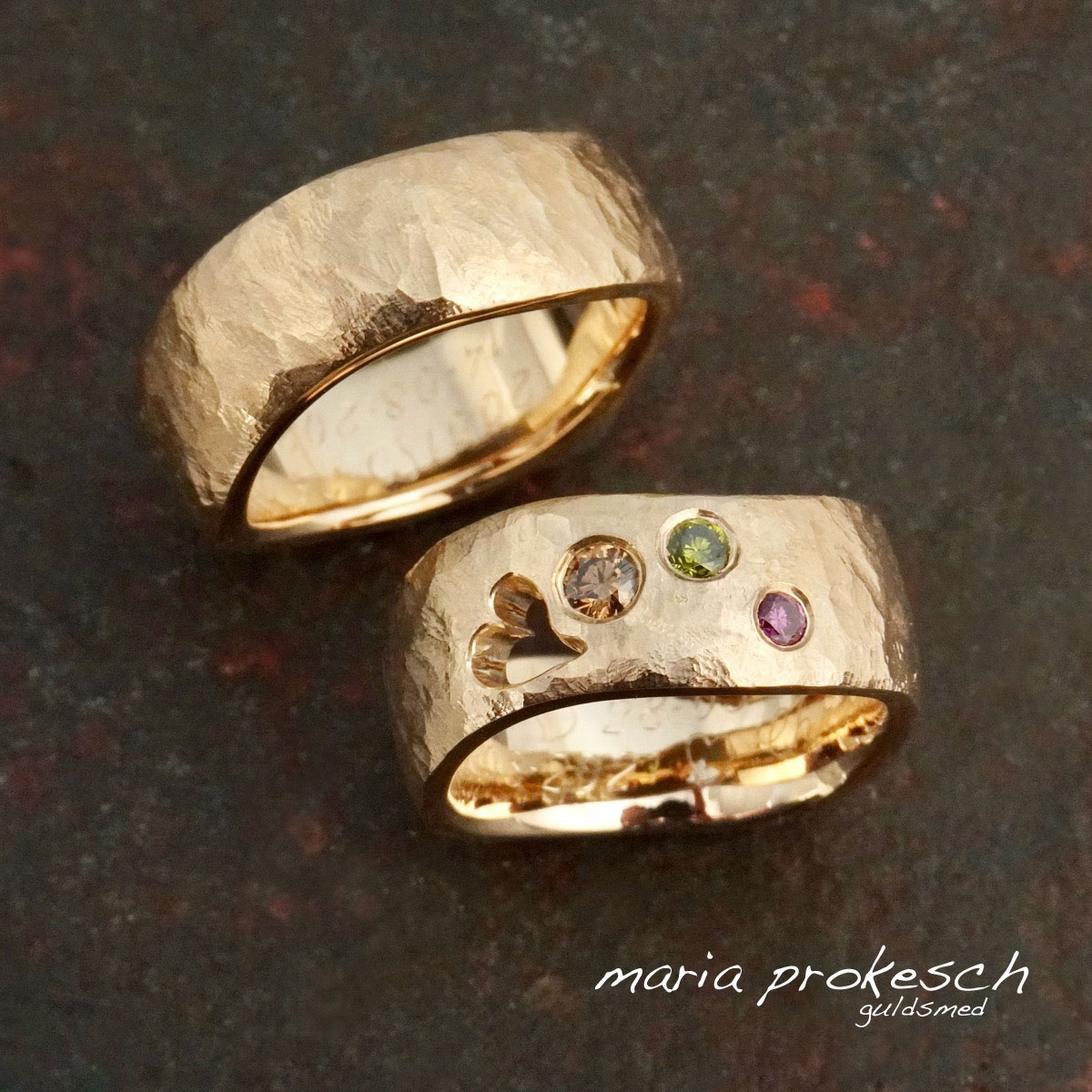 Rustikke vielsesringe i 14 karat guld med farvede sten, behandlede diamanter, strøet. På begge ringe er overfladen rustik ruflet og har en bølgende ringform. Kvinde vielsesring har også et hjerte udsavet.
