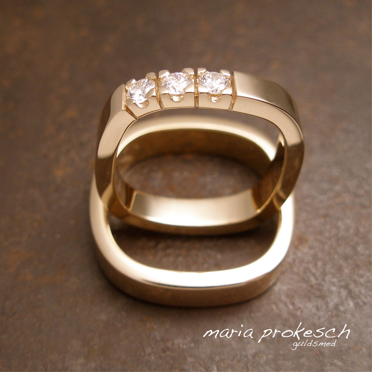 Klassiske vielsesringe i 14 kt rødguld. Ringene er firkantet med runde hjørner. Hendes ring er en alliancering, med 3 brillanter. Stenene sidder smukt asymmetrisk og utraditionelt
