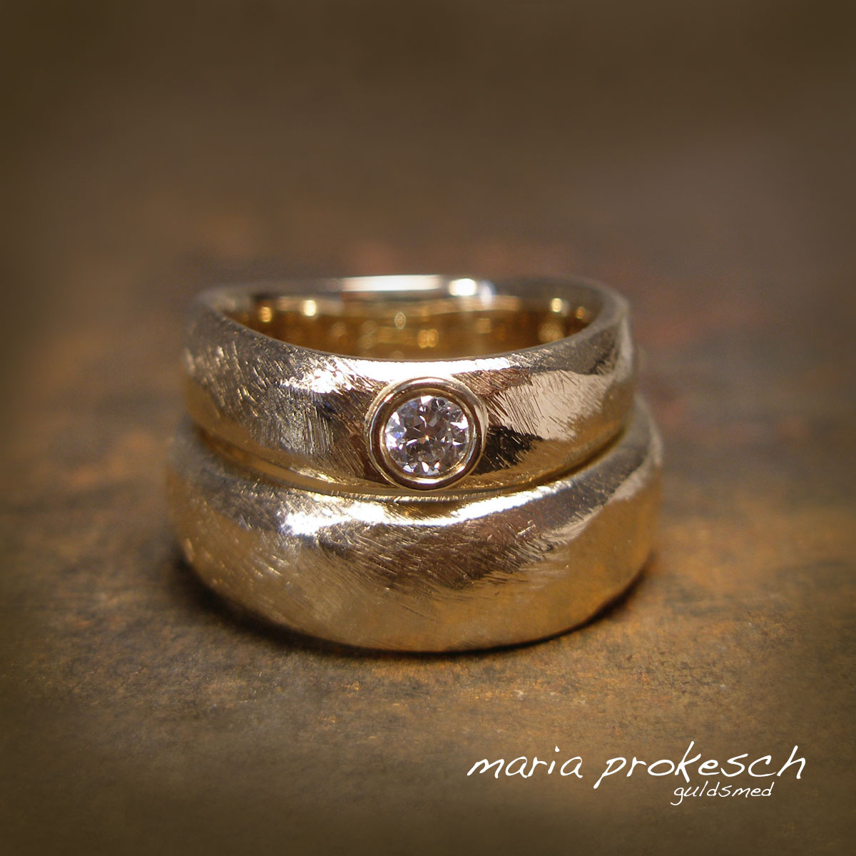 Grovfilede vielsesringe i ekset form, rustik 14 karat guld. Den ekset form gør at ringe sidder rigtigt godt på finger. Kvinde ring med sten, en stor hvid diamant (brillant) i fatning.