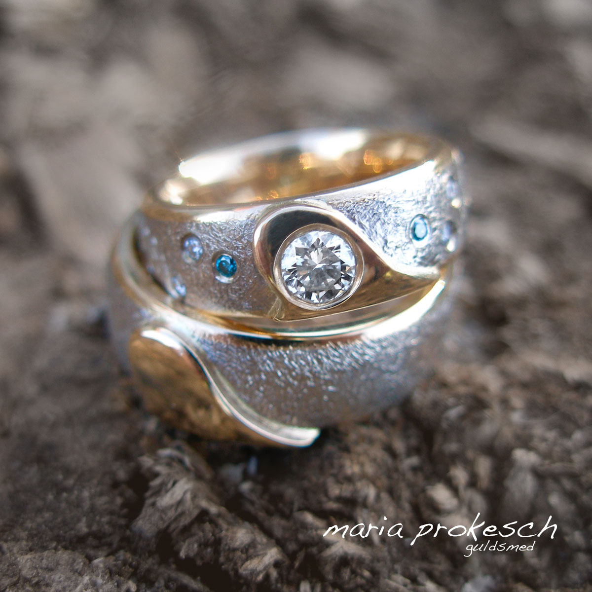 Tofarvede guld, gult guld og hvidguld, i anderledes design. Begge ringe har lidt over et halvt hjerte som en personlig detalje. I hendes ring er der både en stor diamant og flere små sten.