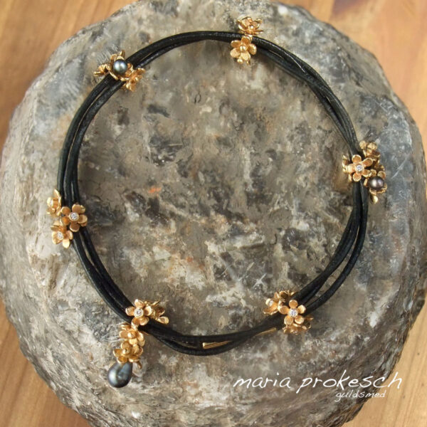 Armbånd med blomster i guld og små keshi tahiti perler og diamanter. Charms som sidder på læder snøre