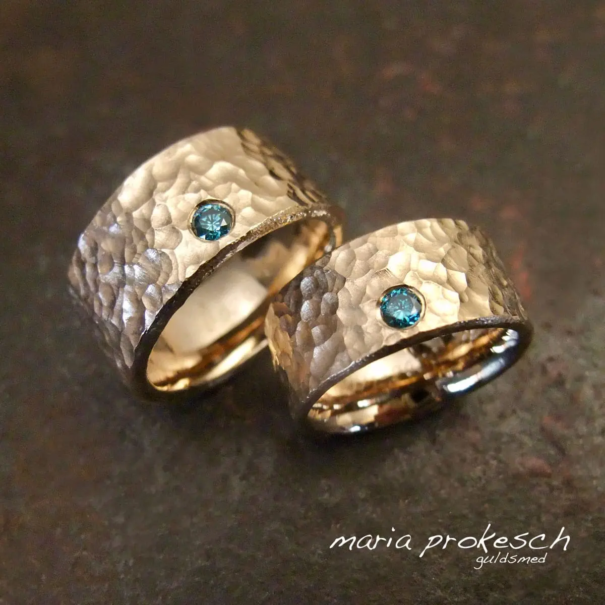 Vielsesringe guld sæt i 14 karat. Brede guldringe med stor blå sten, en diamant. Ringe med rustikke og rå overflade. Vielsesring til kvinde og herrering er ens som par. Design efter ønske, håndlavede af Guldsmed.